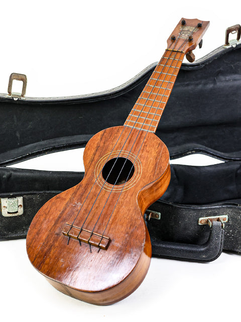 1920s Kumalae ukulele displayed in its case, set on a pristine white background.