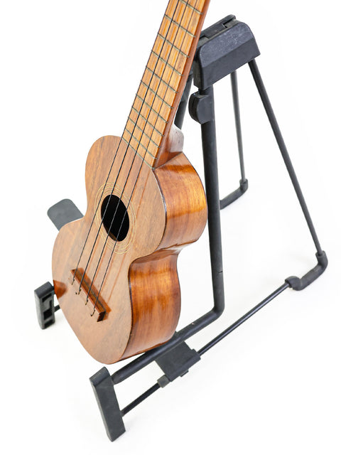 1920s Kumalae ukulele displayed on a sleek black stand, highlighting its rich history and Hawaiian musical heritage.