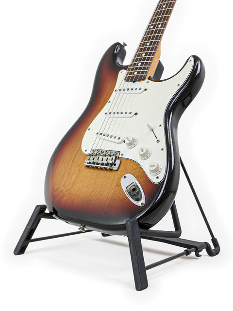 1982 Fender AVRI ‘62 Stratocaster resting on a stand, showcasing its vintage charm against a white background.