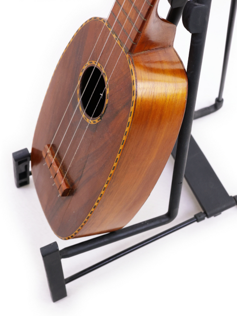 A 1928 Kamaka Pineapple Style #3 ukulele elegantly positioned on a black stand.