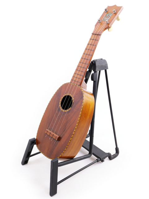 A 1928 vintage Kamaka Pineapple Style #3 ukulele resting on a stand, showcasing its beautiful wooden body.