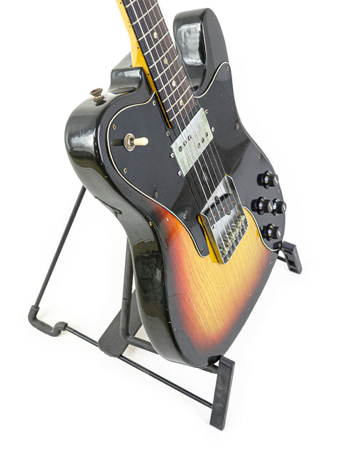  A 1977 Fender Telecaster Custom guitar showcased on a stand, contrasted by a deep black background.
