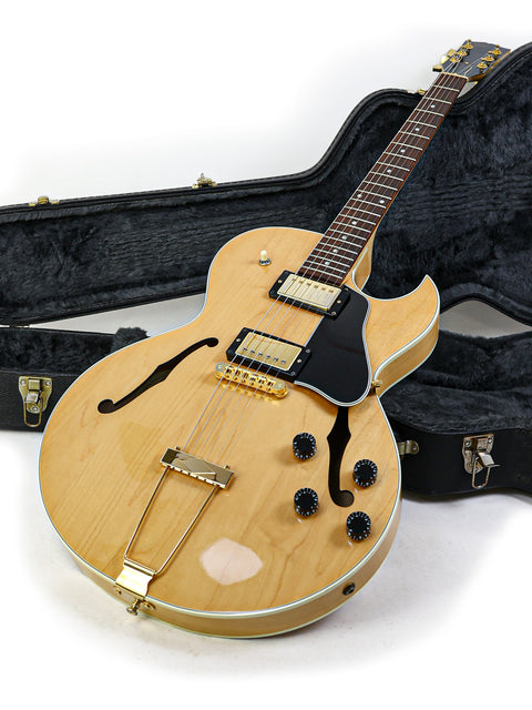 A 2002 Gibson ES-135 guitar in its case, displayed on a pristine white surface, highlighting its classic craftsmanship.
