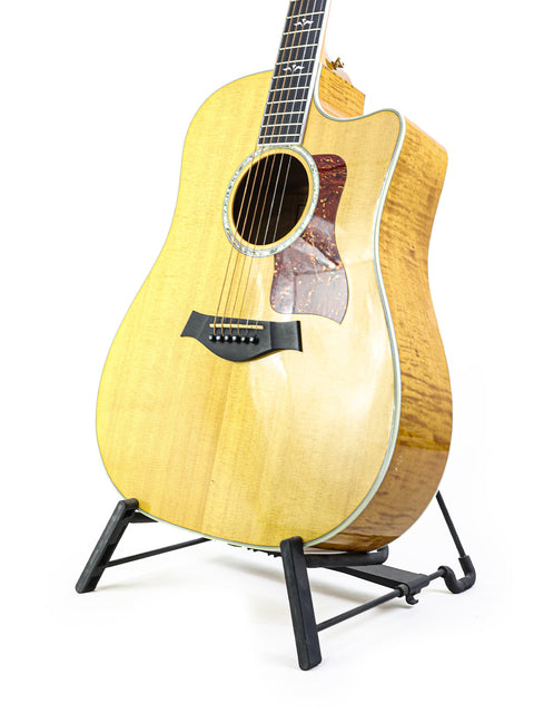 A 2003 Taylor 610CE guitar on a stand, showcasing its beauty against a plain white background.
