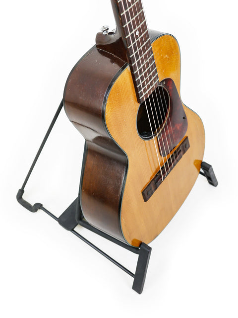 A Kay K113 Parlour guitar from 1966-68 displayed on a stand, featuring a striking contrast against a white backdrop.