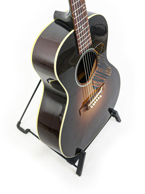 A black acoustic guitar, the Gibson 30s L-00 True Vintage from 2014, elegantly positioned on a stand for display.