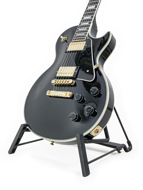 A black electric guitar, the Gibson Les Paul Custom from 2010, elegantly displayed on a stand.