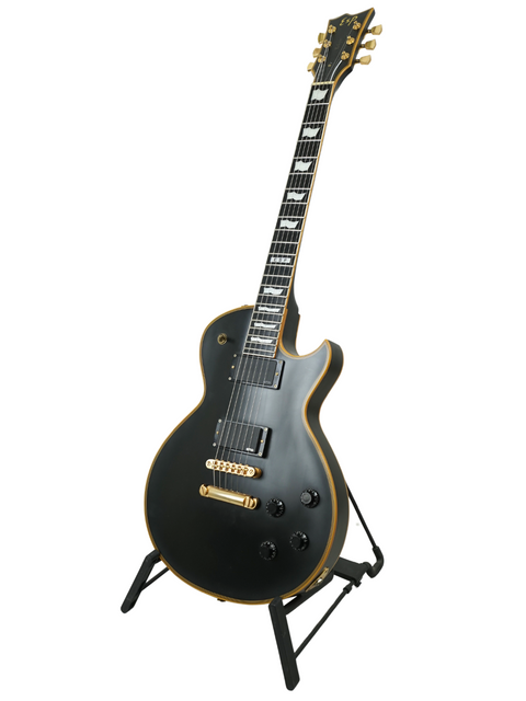 A black electric guitar with gold accents on a stand against a white background.