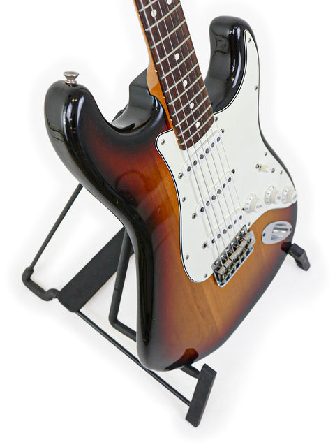 A classic 1982 Fender AVRI ‘62 Stratocaster resting on a stand, highlighted by a dark black backdrop.