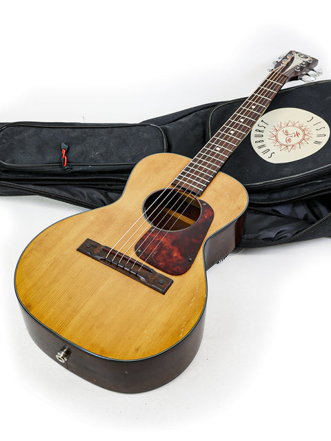  A classic Kay K113 Parlour guitar from the late 1960s, displayed in its case with a guitar strap nearby.