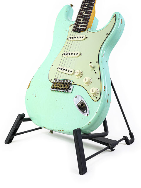 A green ‘59 Stratocaster Relic guitar by Fender, elegantly positioned on a stand with a sleek black base.