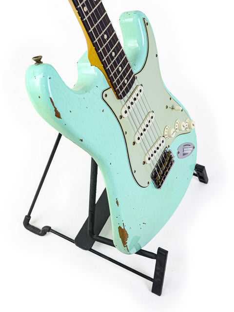 A green Fender Yuriy Shishkov Master Built ‘59 Stratocaster Relic guitar elegantly positioned on a stand with a white backdrop.