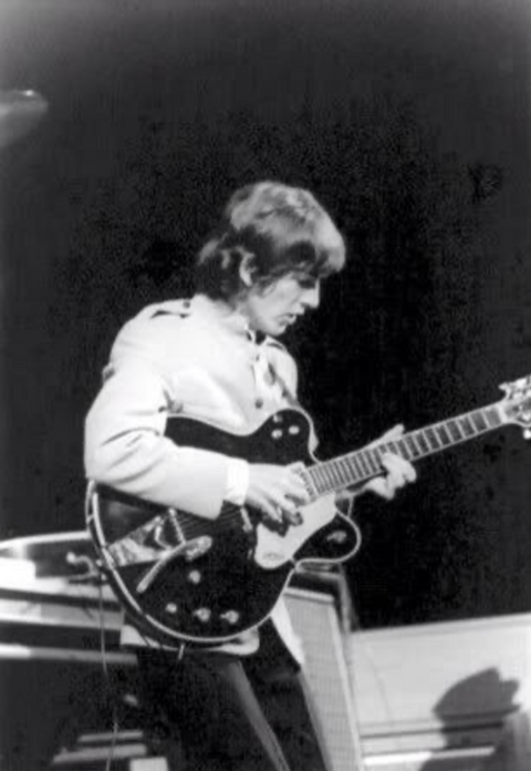 A man dressed in a suit passionately plays a 1967 Gretsch 6122 Chet Atkins electric guitar on stage.