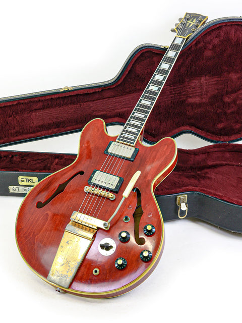 A red 1967 Gibson ES-355 Stereo guitar with its case on the floor, capturing the essence of vintage musical craftsmanship.