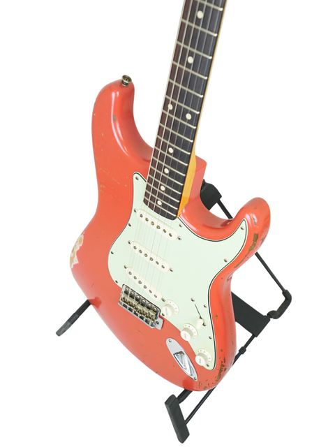  A red Fender Kyle McMillin Masterbuilt 1960 Stratocaster Relic electric guitar displayed on a stand.
