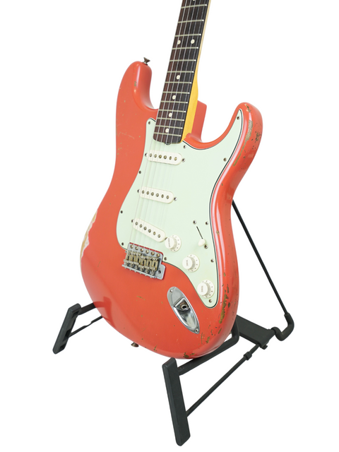 A red guitar, the Fender Kyle McMillin Masterbuilt 1960 Stratocaster Relic, stands out on a stand with a white backdrop.