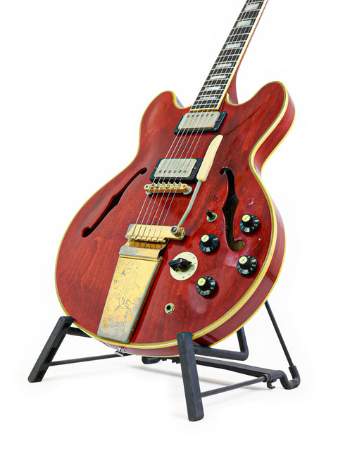 A red vintage Gibson ES-355 Stereo guitar from 1967, beautifully positioned on a stand with a white backdrop.