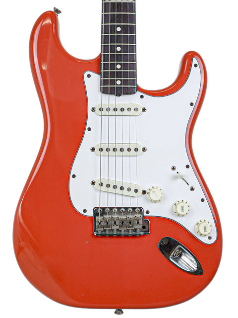 A striking red electric guitar, the vintage Fender AVRI ‘62 Stratocaster from 1982, featuring a sleek white pickguard.
