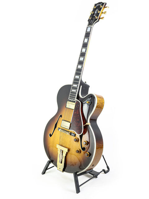 A stunning Gibson L-5 CES guitar with a stand, set against a white backdrop, highlighting its 2002 craftsmanship and beauty.