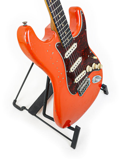 A vibrant red 1963 Fender L-Series Stratocaster guitar elegantly positioned on a black stand, perfect for any music lover.
