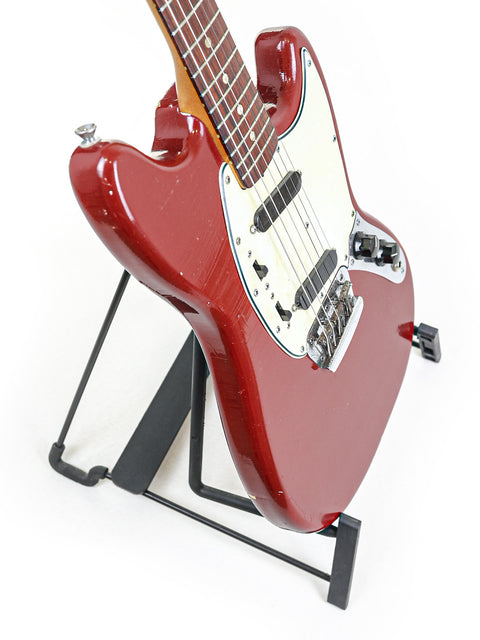 A vibrant red 1966 Fender Musicmaster II guitar on a black stand, highlighting its retro appeal and craftsmanship.