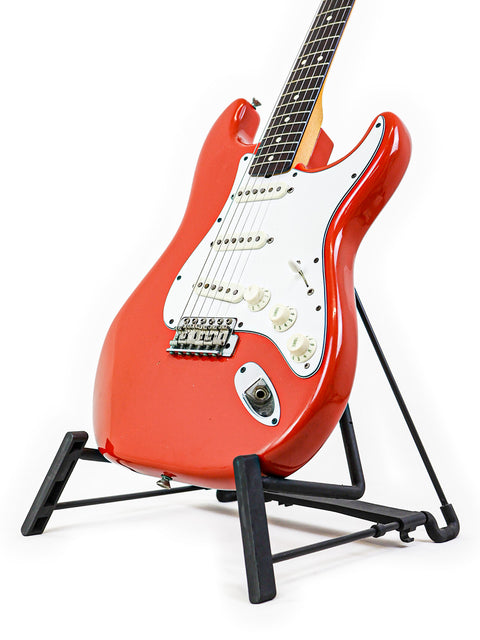 A vibrant red Fender AVRI ‘62 Stratocaster guitar on a stand, showcased with a plain white background.