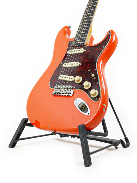 A vibrant red vintage Fender Stratocaster guitar from 1963 on a stand, highlighted by a white background.
