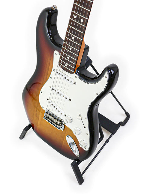 A vintage 1982 Fender AVRI ‘62 Stratocaster guitar on a stand, highlighted by a simple white background.
