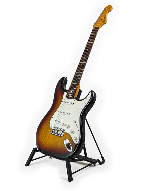  A vintage Fender AVRI ‘62 Stratocaster guitar on a stand against a clean white background.
