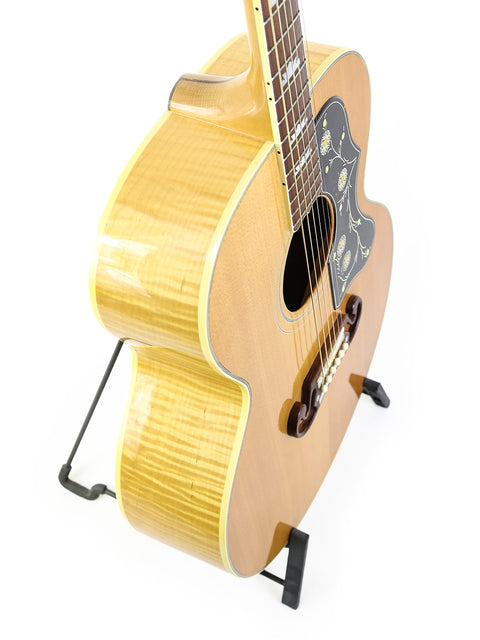 A white background highlights a Gibson SJ-200 guitar from 1999, elegantly positioned on a stand.