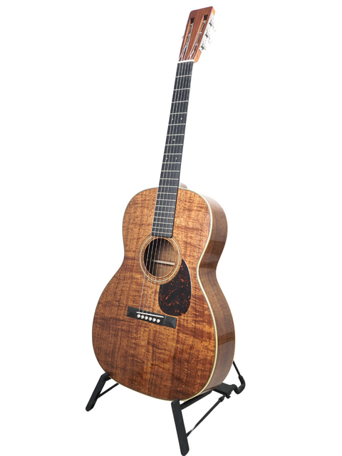 A wooden Martin 000-28K Authentic 1921 guitar displayed on a stand, set against a clean white backdrop.