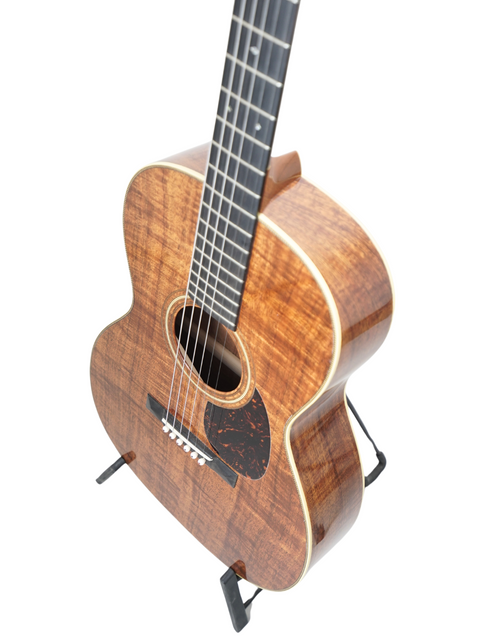 A wooden Martin 000-28K Authentic 1921 guitar elegantly positioned on a black stand, emphasizing its classic style.