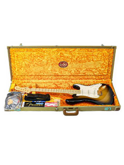 An open guitar case with a yellow lining, displaying a Fender Stratocaster and accessories.