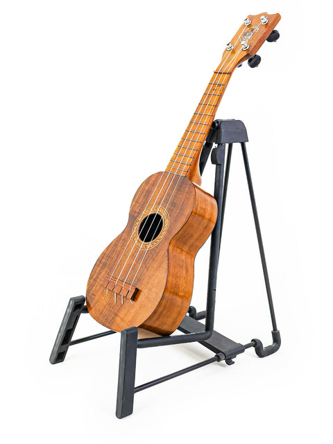 Angled view of the Aloha Tabu Akai ukulele on a stand, emphasizing its elegant design and warm wooden tones.

