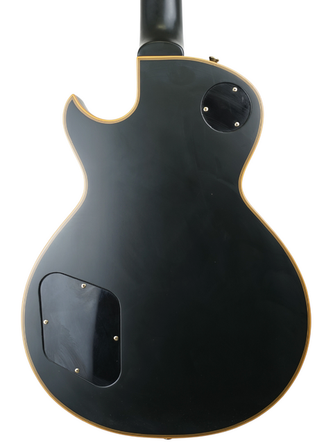 Back of a black electric guitar with access panels visible against a white background.