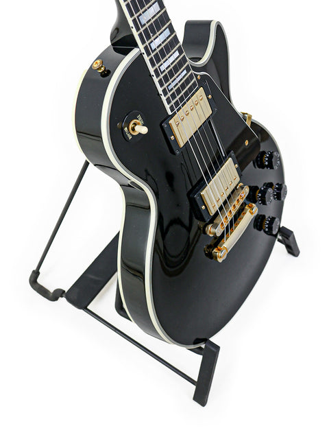 Black Gibson Les Paul Custom electric guitar from 2010, resting on a stand, highlighting its premium features.