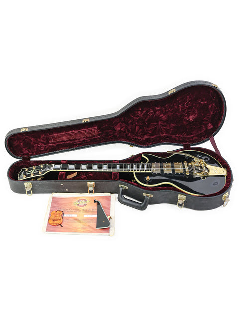 Black Gibson Les Paul Custom guitar from 2004, resting in its case with a guitar pick nearby.