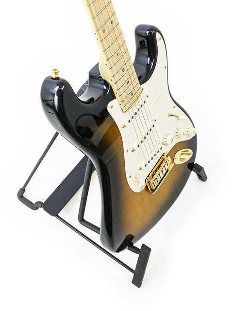 Black and sunburst electric guitar on a stand against a white background.