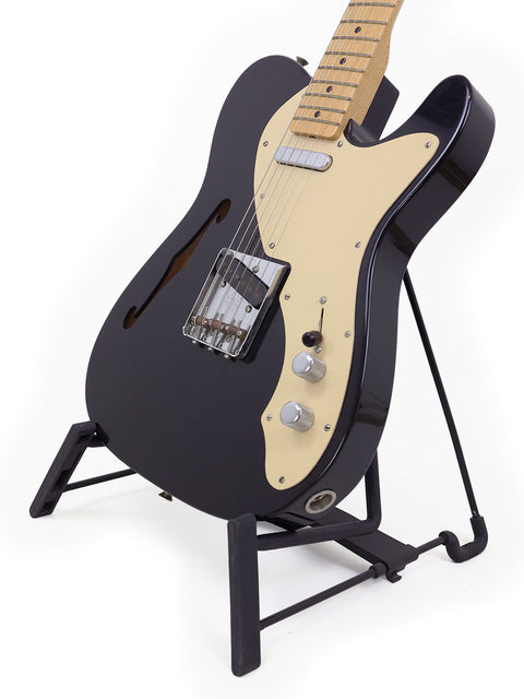 Black electric guitar on a stand, a 2005 Fender Custom Shop Telecaster Thinline, highlighting its vintage appeal.
