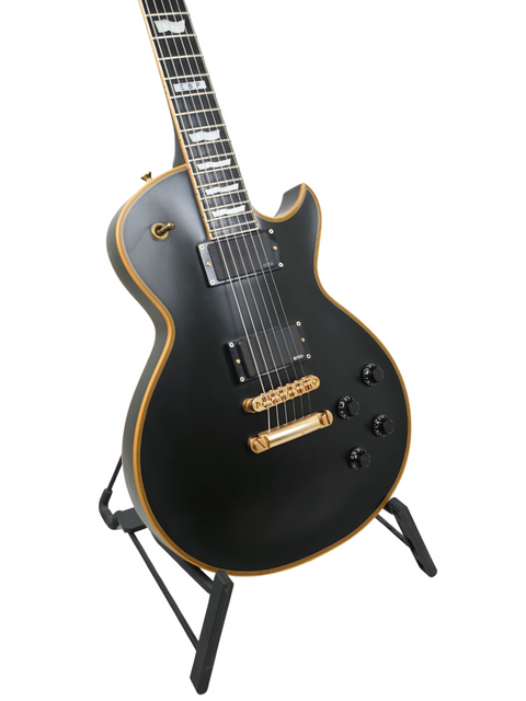 Black electric guitar with gold details on a stand, isolated on a white background.