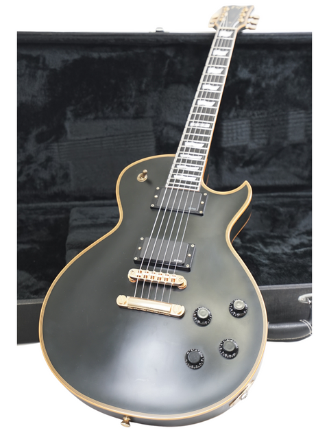 Black electric guitar with gold trim against a dark background.