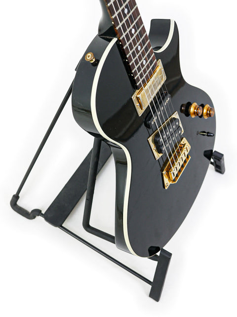 Classic black Gibson Nighthawk guitar from 1999, showcasing a beautiful gold neck on a stand, a must-have for guitar lovers.
