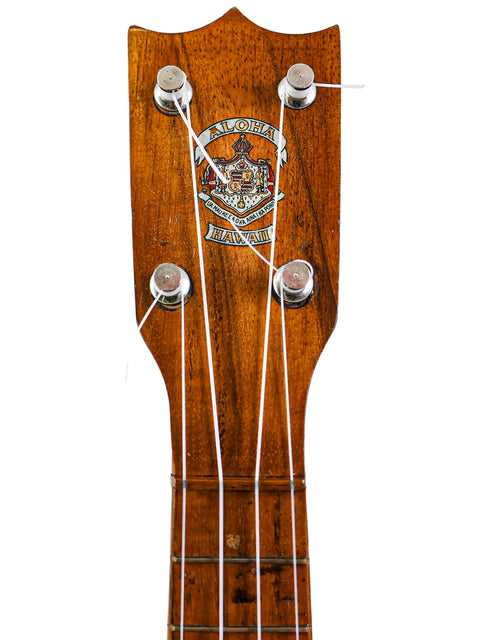 Close-up of the Aloha Tabu Akai ukulele headstock, displaying the Aloha Hawaii logo and original tuning pegs.
