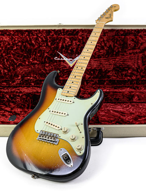 Fender guitar, specifically a John Cruz Master Built ‘64 Stratocaster Relic, resting in a striking red case.