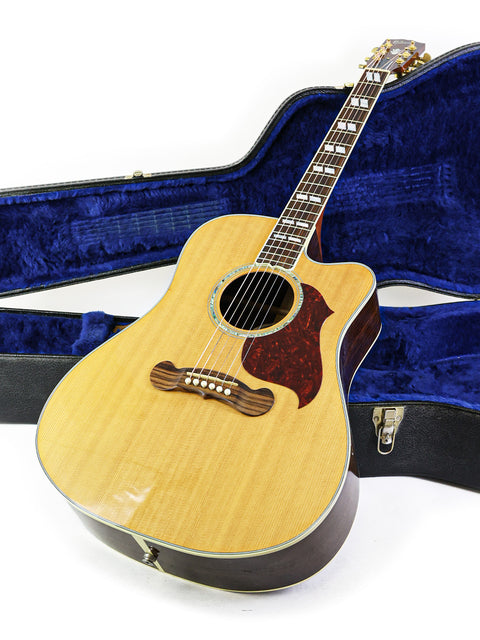 Inside a blue case, a Gibson Songwriter Studio Deluxe EC guitar is displayed, emphasizing its sleek design and premium features.