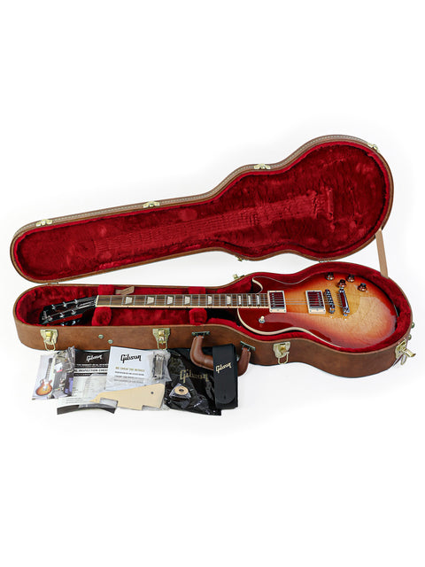 Inside a guitar case, a 2018 Gibson Les Paul Standard rests, complete with a guitar strap, ready for musical adventures.