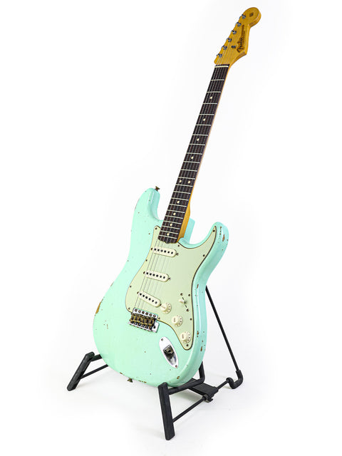 Mint green Fender Yuriy Shishkov Master Built ‘59 Stratocaster Relic guitar elegantly positioned on a stand with a white backdrop.