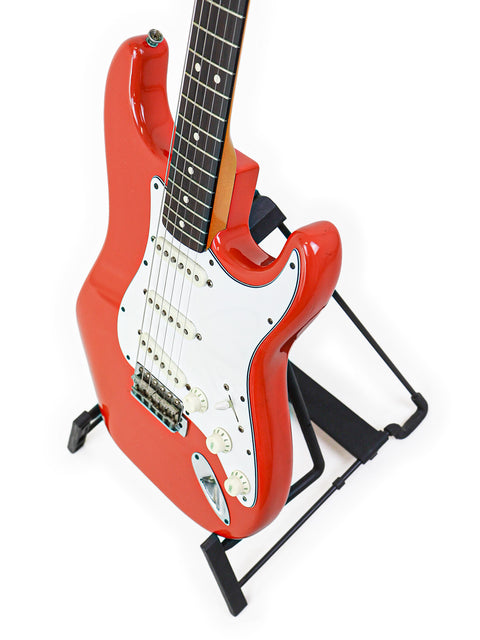 Red Fender AVRI ‘62 Stratocaster guitar displayed on a stand, set against a bright white backdrop.