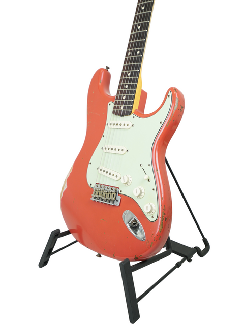 Red Fender Kyle McMillin Masterbuilt 1960 Stratocaster Relic guitar elegantly positioned on a stand with a white background.
