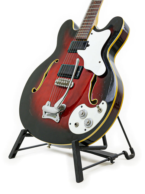 Red and black 1967 Mosrite Celebrity III guitar resting on a stand, showcasing its vintage charm.